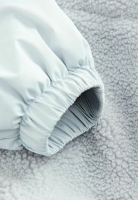 Ljusblått tygärmslut med samlad elastisk öppning på en texturerad grå fleecebakgrund. Tyget verkar slätt, vilket kontrasterar mot fleecen.