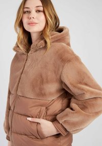 Kurtka pikowana z futerkowym wykończeniem w odcieniach beżu i karmelu. Posiada kaptur, zamek błyskawiczny oraz boczne kieszenie z prążkowanymi mankietami.