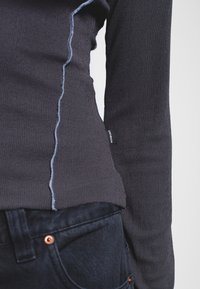 Maglia a maniche lunghe a coste scure con cuciture a contrasto, abbinata a jeans in denim scuri con bottone di rame e tessuto testurizzato.