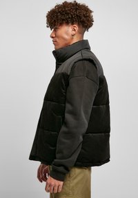 Jachetă puffer neagră cu textură de catifea și umplutură matlasată, având un guler înalt și fermoar frontal. Croi slim cu mâneci lungi.
