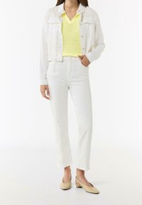 Białe dżinsowe spodnie, biała koszula z guzikami i jasna żółta sweterkowa bluzka. Beżowe buty na niskim obcasie dopełniają strój.