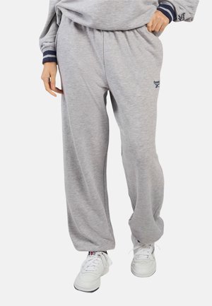 Persoon draagt losse grijze trainingsbroek met Reebok-logo, gecombineerd met witte sneakers en een bijpassend grijs sweatshirt.