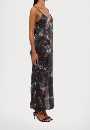 Femme en robe maxi noire sans manches avec imprimé galaxie et sandales à talons noires avec brides à la cheville.