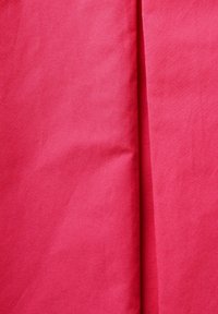 Kirkas vaaleanpunainen kangas, jossa on sileä rakenne, sisältää hienovaraisia ryppyjä ja laskoksia. Materiaali näyttää kevyeltä ja valuu pehmeästi.