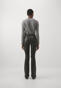 Maglione grigio a coste e pantaloni in pelle nera a ampia gonna. Il maglione ha maniche lunghe; i pantaloni sono attillati con tasche e una finitura liscia.