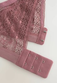 Mauve čipkasta naramenica s cvjetnim uzorcima i zatvaranjem na tri reda i dva stupca s kukama na bijeloj pozadini.