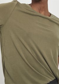 Oliven grøn, kortærmet t-shirt lavet af blødt bomuldsstof med en afslappet pasform og v-hals, der har en subtil tekstur og drapering.