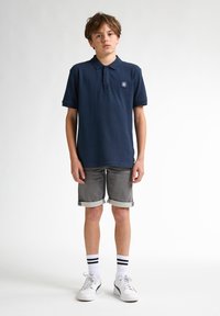 Marinblå polo, gråta rullade shorts, vita sneakers med svarta accenter och knälånga vita strumpor med svarta ränder. Enkel, avslappnad design.