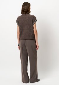 Bruine gebreide top met een geribbelde textuur en korte mouwen, met een decoratieve kettingrand bij de halslijn. Gecombineerd met losse, taupe broeken.