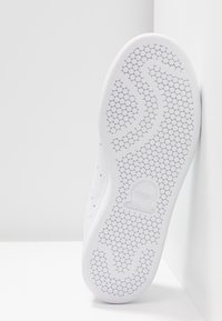 Semelle de chaussure de sport blanche avec un motif de traction hexagonal, dotée d'un logo Adidas moulé et d'un matériau synthétique lisse.