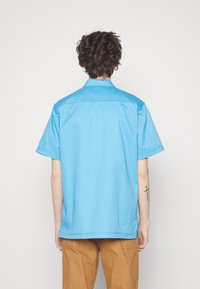 Korte mouwen shirt van effen lichtblauwe katoen met een standaard kraag en een rechte zoom. Bevat subtiele zijsplitten.