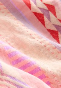 Tissu doux avec des motifs géométriques rose, violet et rouge et des coutures visibles, montrant la texture et les détails tissés.