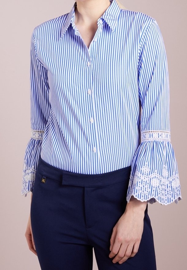 Randig blå och vit knapp-up skjorta med utsvängda ärmar som har spetsdetaljer, i kombination med mörka byxor. Skräddarsydd passform i bomullsmaterial.