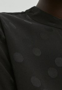Černý látkový top s jemným texturovaným vzorem různě velkých tónovaných kruhů, s hladkým povrchem a jednoduchým designem s kulatým výstřihem.