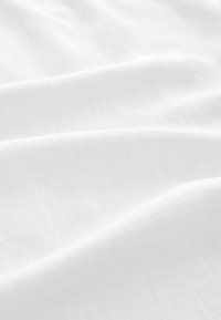 Biely textil s hladkým, mierne textúrovaným povrchom, ktorý má jemné vrásky a ľahký, vzdušný vzhľad.