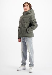 Groene pufferjack met capuchon, voorzien van een geborduurd ontwerp en zijzakken. Gecombineerd met lichtblauwe versleten jeans en witte sneakers.