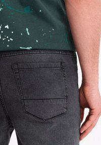 Jeans de mezclilla gris con un primer plano del bolsillo trasero, que presenta un diseño simple y costuras en contraste. La cintura es visible en la parte superior.