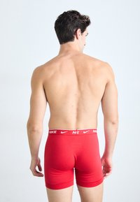 Rode katoenen boxershorts met een witte Nike-logo tailleband, met een aansluitend ontwerp en een gladde textuur. Uitzicht van achteren.