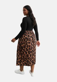 Abito con stampa leopardata, dotato di una parte superiore nera aderente e una gonna fluida di lunghezza midi. Tessuto morbido, vita elastica, abbinato a sneakers bianche.