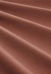 Tessuto terracotta con una superficie liscia e leggermente strutturata, caratterizzato da pieghe dolci e da un colore uniforme in tutto il tessuto.