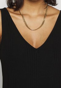 Czarny prążkowany top bez rękawów z dekoltem w kształcie litery V, zdobiony złotym naszyjnikiem w ogniwowym wzorze dla dodatkowego akcentu.