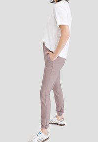 Ljust rosa stretchbyxor med slim fit, nedtill med mudd, framfickor och en liten logo vid midjan, kombinerat med en vit t-shirt och sneakers.