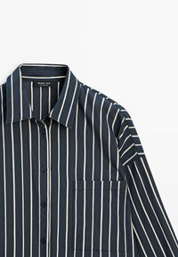 Marineblaues Hemd mit hellen vertikalen Streifen, ausgestattet mit spitzem Kragen, Knopfleiste vorne und Brusttasche. Glatter Stoff mit strukturierter Passform.