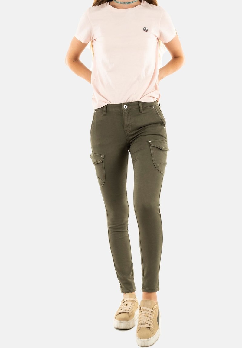 Pantalons cargo verts avec poches, assortis à un t-shirt rose clair arborant un petit logo. Les chaussures sont beiges, avec un design texturé.