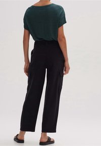 Chemise à manches courtes vert foncé avec poignets roulés, associée à un pantalon noir taille haute doté de poches latérales et d'une coupe droite.