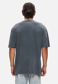 Grå t-shirt med kort ärm, avslappnad passform och rundad halsringning, tillverkad av mjuk bomull. Har en enkel baksida med minimal sömnadsdetalj.