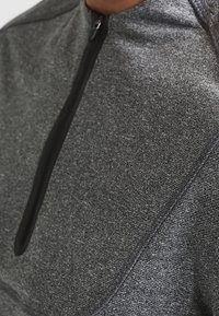 Top deportivo con cremallera hasta un cuarto en gris oscuro, con una tela texturizada, cremallera negra y costuras de contraste a lo largo de las costuras.