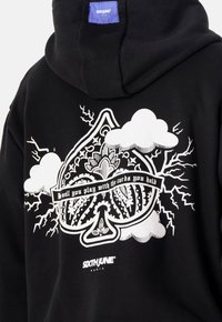 Sudadera negra con capucha que presenta un gran diseño gráfico en blanco con nubes y relámpagos, texto que dice "Bueno, juegas con las cartas que tienes" y el logo de la marca.