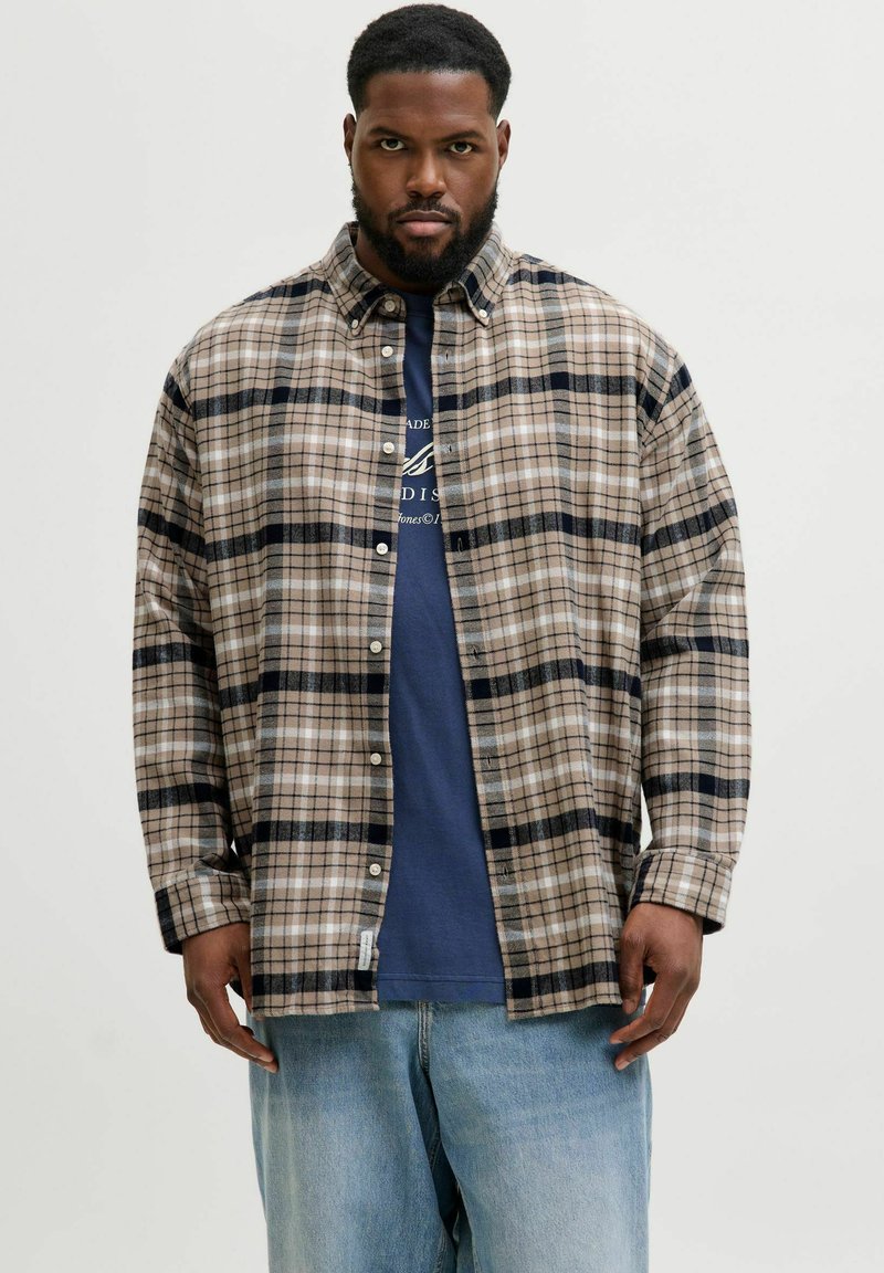 Beige, braun und marineblau kariertes Flanellhemd mit Button-Down-Kragen, langen Ärmeln und einer lockeren Passform über einem marineblauen T-Shirt.