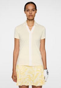 Koszulka polo w jasnym żółtym kolorze z krótkimi rękawami, dekoltem w serek oraz białymi paskami na środku, zestawiona z żółtą spódnicą w wzory.