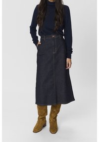 Jeanskjol i mörkblått, lång och A-linjeformad, med framfickor och kontrasterande sömmar. Bärs med en marinblå polotröja och tanfärgade mockastövlar.