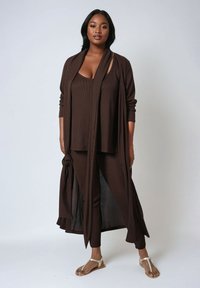 Brown two-piece outfit with a long, open cardigan and fitted top, complemented by matching pants. The fabric has a ribbed texture.