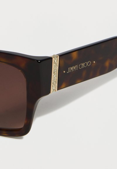 Βραχίονας ορθογώνιων γυαλιών ηλίου με σχέδιο χελώνας, έντονο χρυσό γκλίτερ και λογότυπο «JIMMY CHOO» σε χρυσά γράμματα.