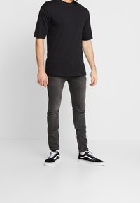 Svart bomull t-shirt med kort ärm, kombinerad med mörkgrå skinny jeans och svarta sneakers med vit sula och snören.