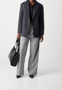 Skräddarsydd svartrandig kavaj över en svart polo, tillsammans med ljusgrå vida byxor och svarta spetsiga klackar. Svart läderhandväska ingår.