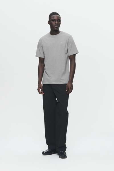 Gray cotton t-shirt with a crew neck and short sleeves, paired with black loose-fit trousers and black shoes. Simple, minimal design.