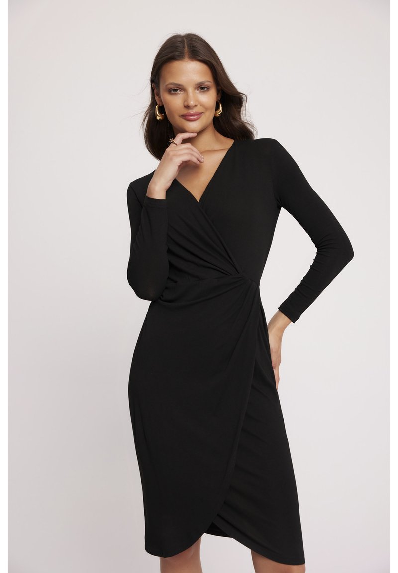 Czarna sukienka z długim rękawem, dekoltem w kształcie litery V i skręceniem w talii, wykonana z gładkiego, elastycznego materiału, sięgająca do kolan.