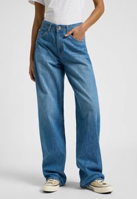 Jeans de tiro alto en denim de color azul claro y corte amplio, con cierre de botón y bolsillos delanteros. Tejido texturado con un ligero desgastado.
