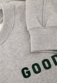 Sudadera gris con cuello redondo, con un estampado texturizado verde que dice "GOOD" en el frente y puños texturizados. Tela de mezcla de algodón, textura suave.