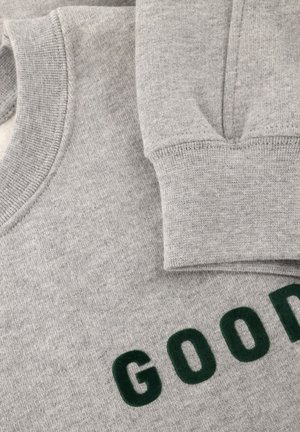 Grå sweatshirt med rund hals, med ett texturerat grönt "GOOD"-tryck på framsidan och texturerade muddar. Tyg av bomullsblandning, mjuk textur.