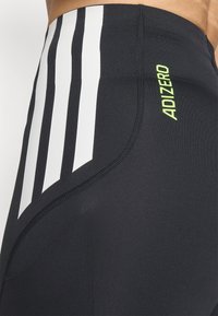 Schwarze Sportleggings mit drei weißen vertikalen Streifen an der Seite und einem limonengrünen "ADIZERO"-Logo. Glattes, dehnbares Material.