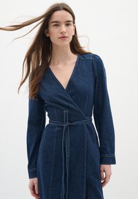 Jeanswrapklänning med långa ärmar, djup V-ringning, bälte i midjan och synlig sömnad. Mörkblå färg med mjuk textur.