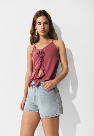 Top halter en color malva con detalle de volantes y una apertura frontal, combinado con shorts de mezclilla de tiro alto en color azul claro. Tejido suave, ajuste casual.