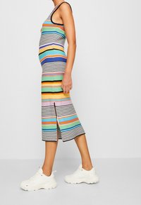 Robe rayée multicolore avec une silhouette ajustée, longueur au genou, fente latérale, texture côtelée, associée à des baskets blanches.