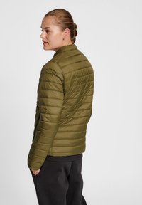 Veste matelassée vert olive avec des coutures horizontales. Dotée d'un col montant et d'une coupe ajustée. Fabriquée en matériau lisse et résistant à l'eau.