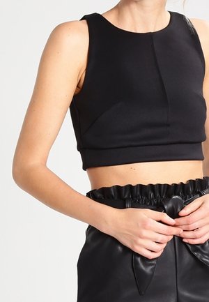 Vrouw draagt een zwart mouwloos cropped top en zwarte leren shorts met hoge taille, een gerimpelde tailleband en een strikceintuur.